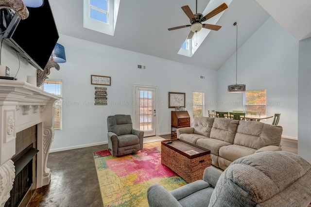 living room featuring ceiling fan, a skylight, a tiled fireplace, and high vaulted ceiling