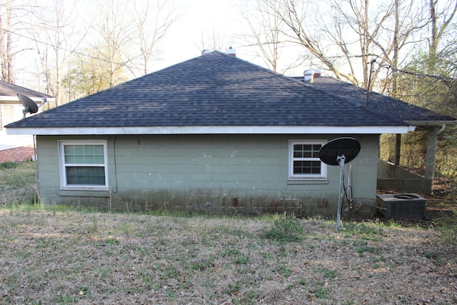 view of side of property featuring concrete block siding, central air condition unit, roof with shingles, and a chimney