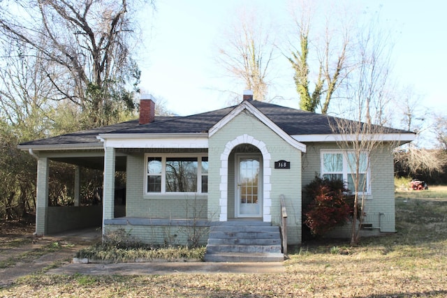 bungalow-style home featuring a carport, brick siding, and a chimney