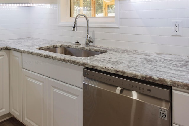 kitchen with light stone countertops, dishwasher, white cabinets, and sink