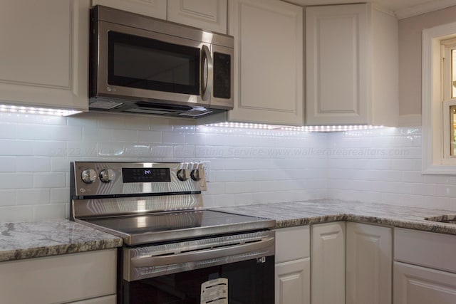 kitchen featuring appliances with stainless steel finishes, backsplash, white cabinetry, and light stone counters