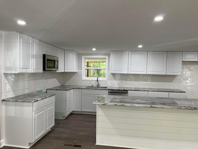 kitchen with appliances with stainless steel finishes, dark hardwood / wood-style flooring, sink, stone countertops, and white cabinetry