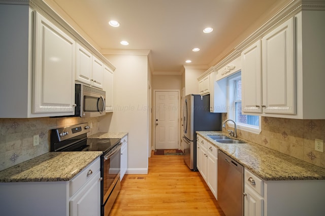 kitchen with stainless steel appliances, sink, white cabinets, and light hardwood / wood-style flooring