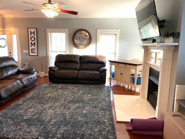 living room featuring wood-type flooring, ceiling fan, and crown molding