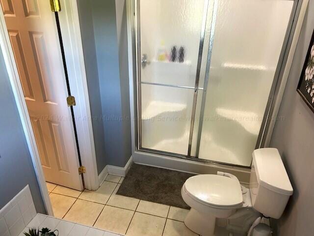 bathroom featuring tile patterned flooring, toilet, and a shower with shower door