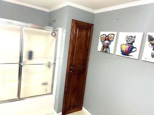 bathroom featuring bath / shower combo with glass door and crown molding