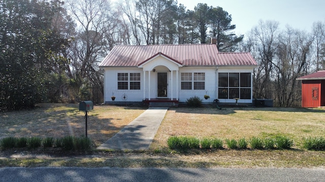 view of front of property featuring a chimney, metal roof, and a front lawn