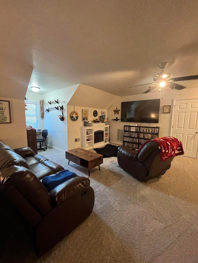 living room featuring a textured ceiling, ceiling fan, a fireplace with raised hearth, lofted ceiling, and carpet