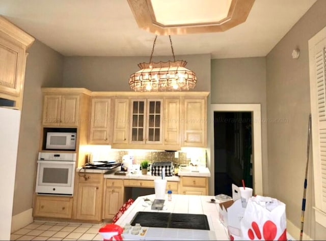 kitchen featuring light brown cabinets, light tile patterned flooring, hanging light fixtures, and white appliances