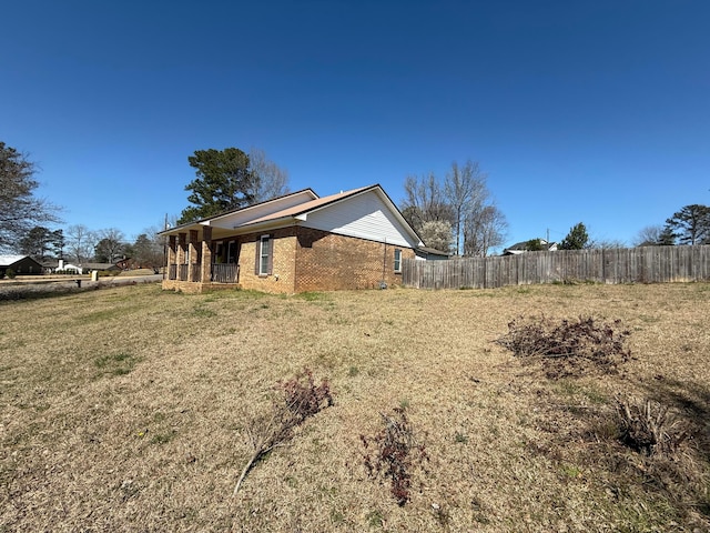 view of property exterior featuring brick siding, a lawn, and fence