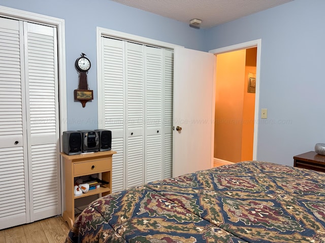 bedroom with light wood-type flooring, two closets, and a textured ceiling