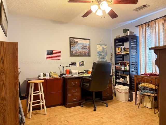 office area with light wood-type flooring, visible vents, a textured ceiling, and a ceiling fan