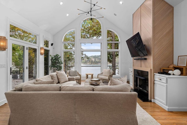 living room with french doors, a large fireplace, vaulted ceiling, an inviting chandelier, and light hardwood / wood-style flooring