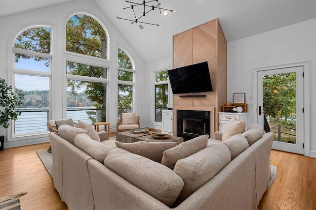 living room featuring a tile fireplace, light hardwood / wood-style floors, high vaulted ceiling, and a chandelier