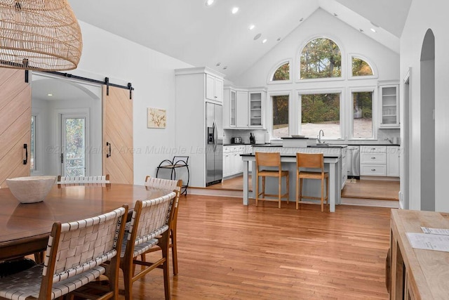 dining space with a barn door, sink, high vaulted ceiling, and light hardwood / wood-style floors