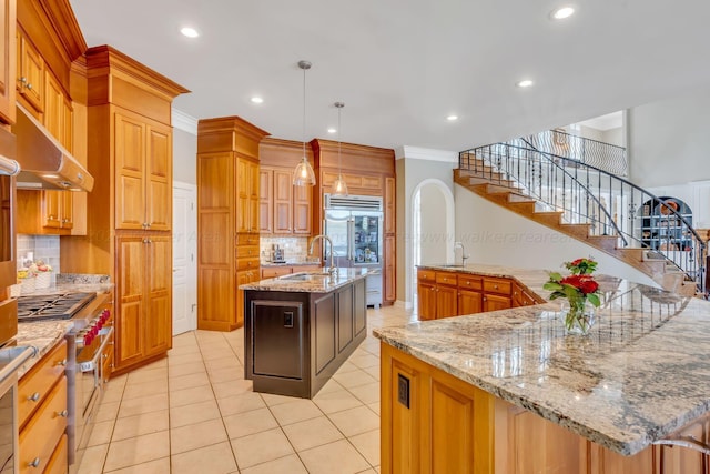 kitchen with backsplash, light stone counters, ornamental molding, a center island with sink, and hanging light fixtures