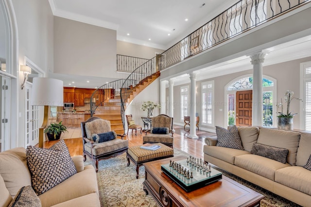 living room with ornate columns, crown molding, a high ceiling, and light hardwood / wood-style flooring