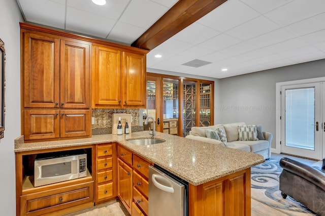 kitchen with stainless steel microwave, backsplash, sink, light stone countertops, and kitchen peninsula