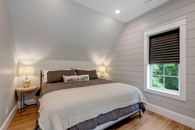 bedroom featuring vaulted ceiling, wood walls, wood finished floors, and baseboards