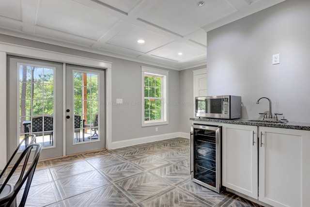 kitchen with beverage cooler, baseboards, stainless steel microwave, french doors, and a sink