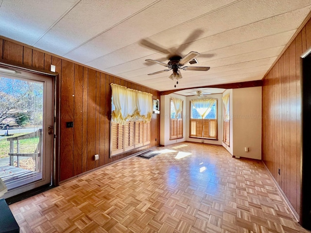 interior space featuring ceiling fan, a healthy amount of sunlight, and wooden walls