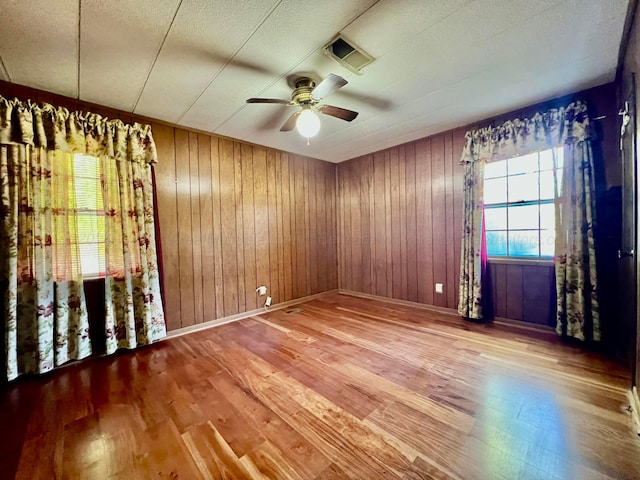 spare room with wood-type flooring, ceiling fan, and wooden walls