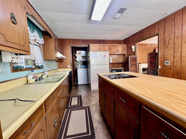 kitchen with sink, white fridge, washer / dryer, wooden walls, and black electric stovetop