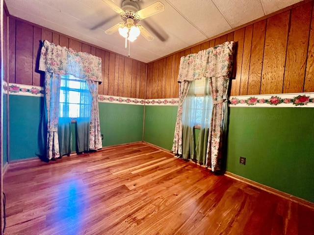 empty room featuring hardwood / wood-style flooring, ceiling fan, a healthy amount of sunlight, and wood walls