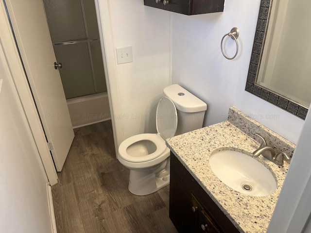 bathroom featuring combined bath / shower with glass door, toilet, vanity, and wood finished floors