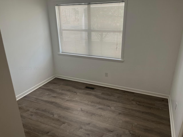 unfurnished room featuring dark wood-type flooring, plenty of natural light, baseboards, and visible vents