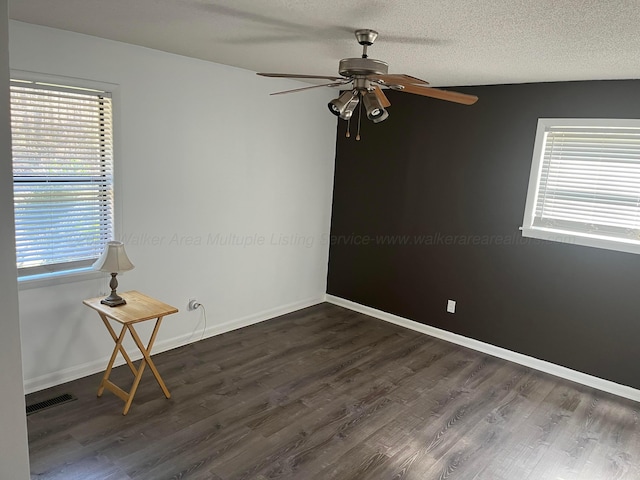 empty room with visible vents, dark wood-type flooring, a textured ceiling, baseboards, and ceiling fan