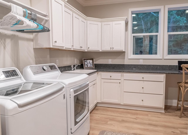 clothes washing area featuring sink, light wood-type flooring, washer and clothes dryer, ornamental molding, and cabinets