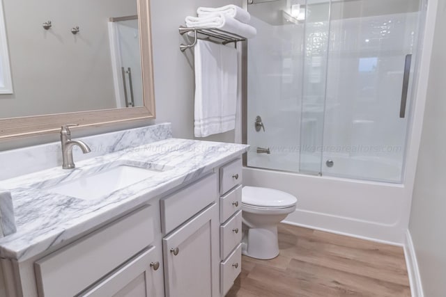 full bathroom with bath / shower combo with glass door, hardwood / wood-style floors, toilet, and vanity