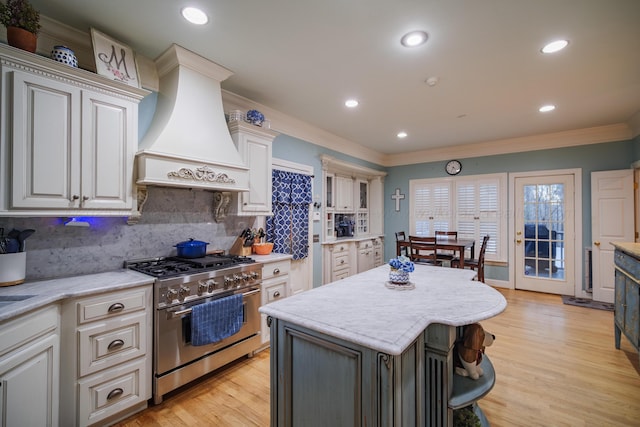 kitchen featuring a center island, light hardwood / wood-style floors, decorative backsplash, high end range, and custom exhaust hood