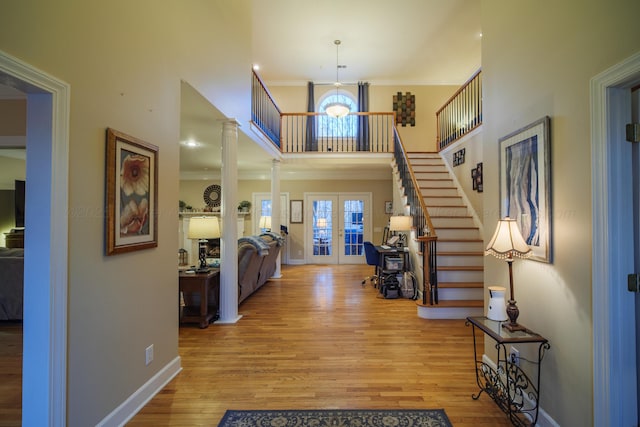 entryway with french doors, light hardwood / wood-style flooring, ornamental molding, a towering ceiling, and decorative columns