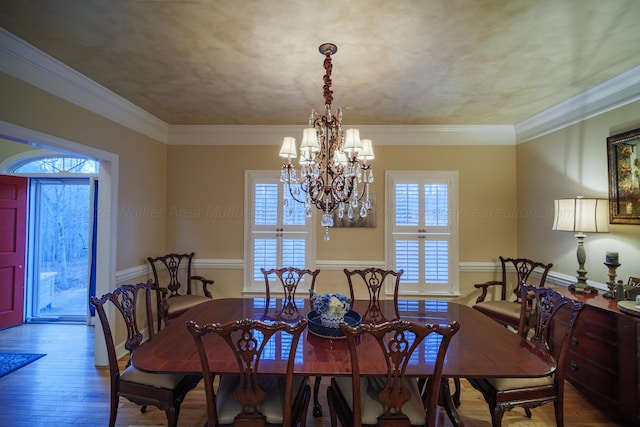 dining space with hardwood / wood-style floors, ornamental molding, and a notable chandelier