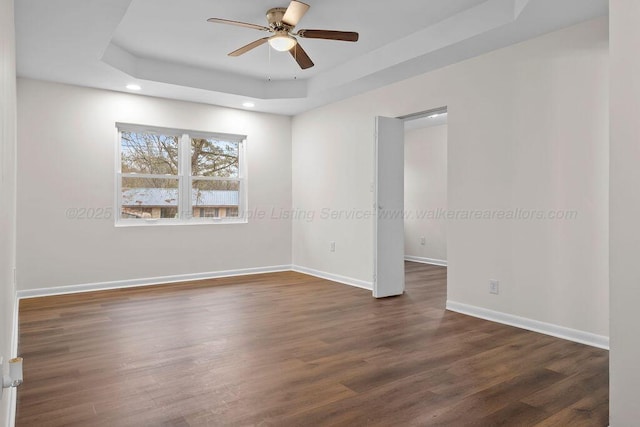 unfurnished room with a raised ceiling, a ceiling fan, dark wood-style floors, recessed lighting, and baseboards