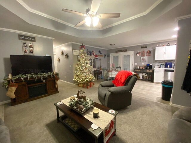 carpeted living room with a raised ceiling, ceiling fan, and crown molding