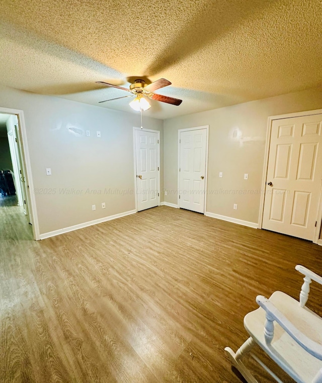 interior space with a textured ceiling, wood finished floors, a ceiling fan, and baseboards