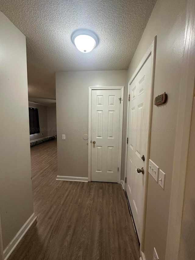 hall with dark wood-style floors, a textured ceiling, and baseboards