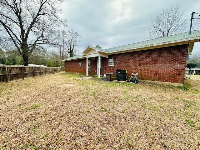 view of home's exterior featuring metal roof, brick siding, fence, and a lawn