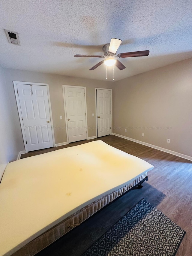 unfurnished bedroom featuring dark wood-style floors, visible vents, a textured ceiling, and baseboards