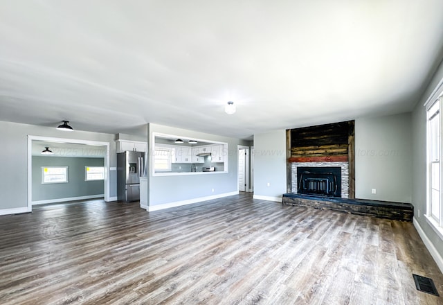 unfurnished living room with dark wood-style floors, a fireplace, visible vents, and baseboards