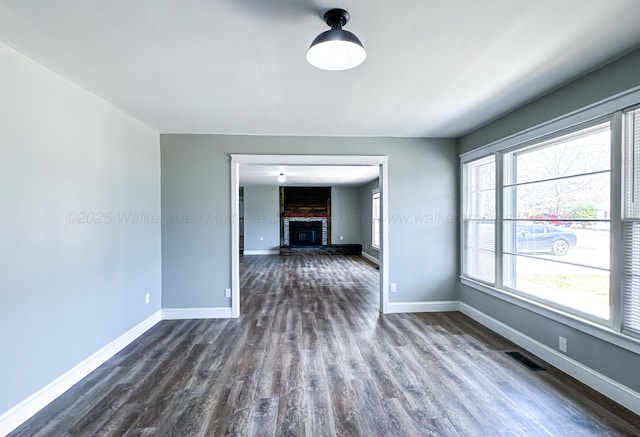 spare room with dark wood-style floors, a brick fireplace, visible vents, and baseboards