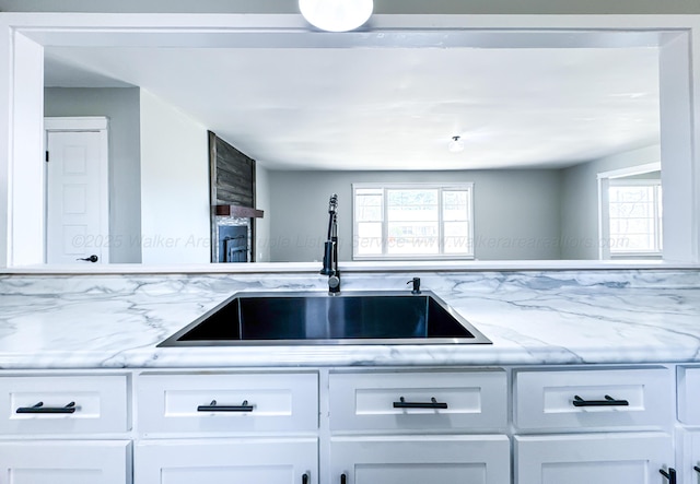 kitchen featuring light stone counters, a healthy amount of sunlight, a sink, and white cabinetry