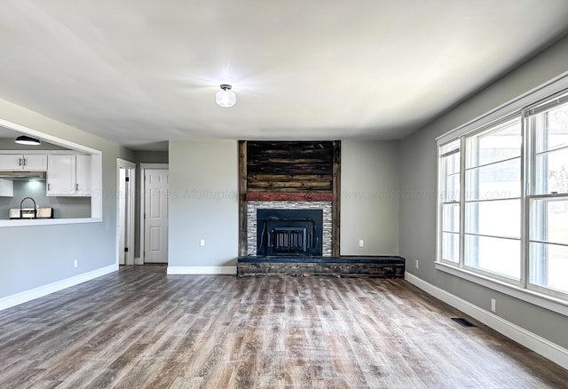 unfurnished living room featuring visible vents, a fireplace, baseboards, and wood finished floors