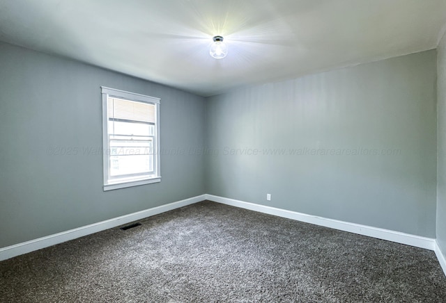 empty room with dark colored carpet, visible vents, and baseboards