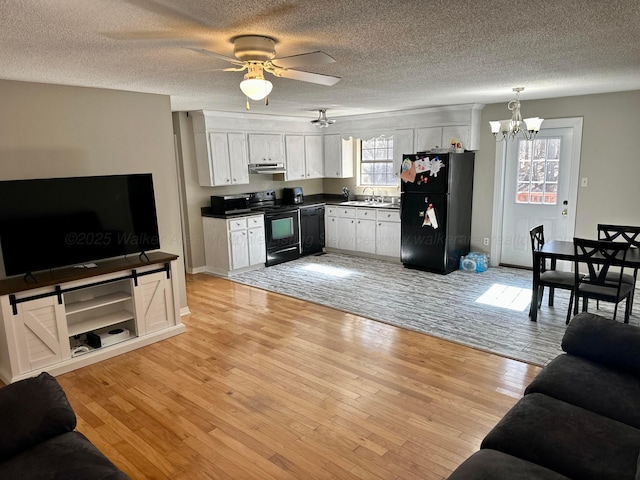 living area featuring ceiling fan with notable chandelier, light wood finished floors, a textured ceiling, and baseboards