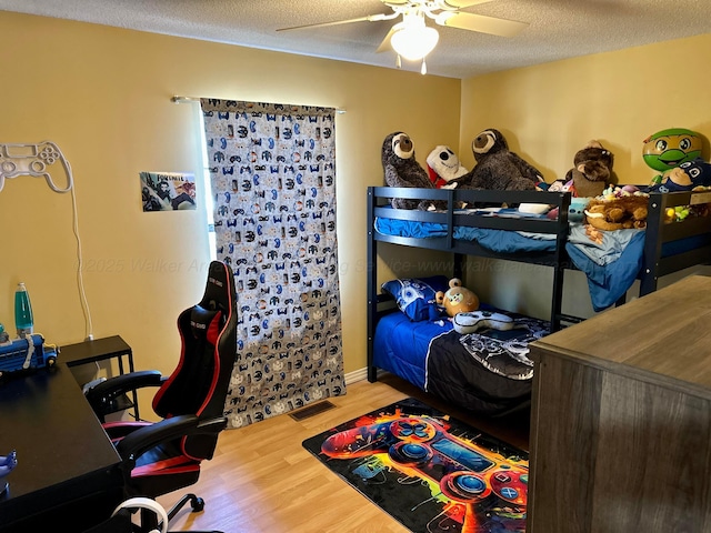 bedroom with ceiling fan, a textured ceiling, visible vents, and wood finished floors