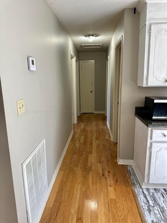 corridor with a textured ceiling, baseboards, visible vents, and light wood-style floors